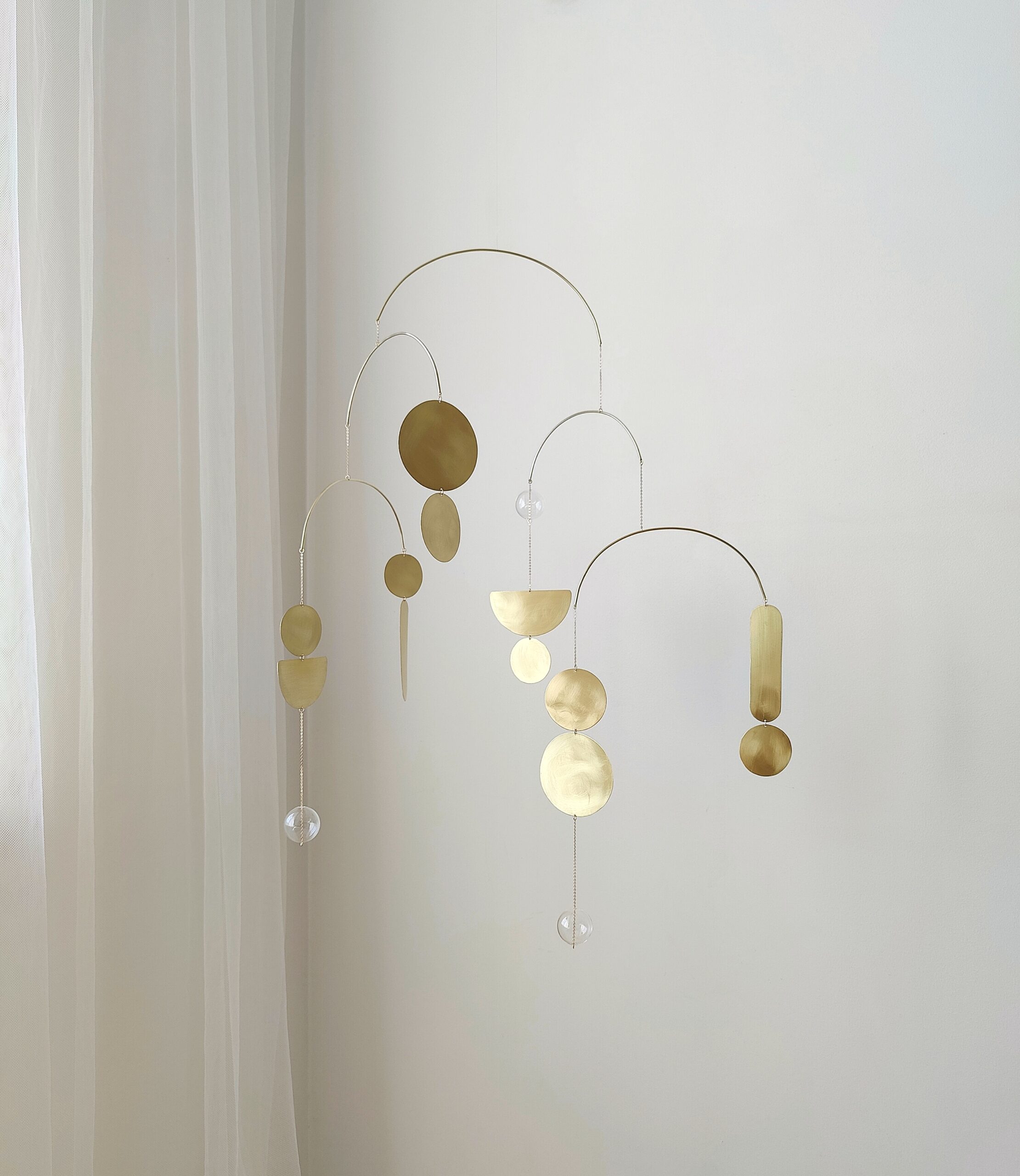 Brass kinetic mobile with geometric shapes reflecting sunlight on white wall - modern art decor for home and office interior