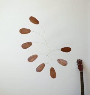 Wooden kinetic mobile made of oak wood in brown color with brass arches hanging in front of white wall - simple and minimalist